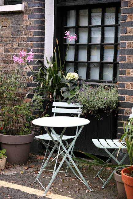 A small, well-maintained terrace garden featuring a white wooden vertical planter with multiple tiers of lush green plants, including trailing foliage and small flowering species, set against a backdr